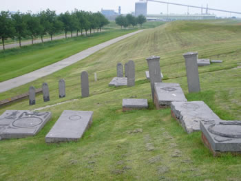 Het gereconstrueerde kerkhof op de dijk naar het westen. Op de achtergrond de industrie met de Aldel (afgebroken 2023/2024). Foto: Caseman, 20 juni 2007.